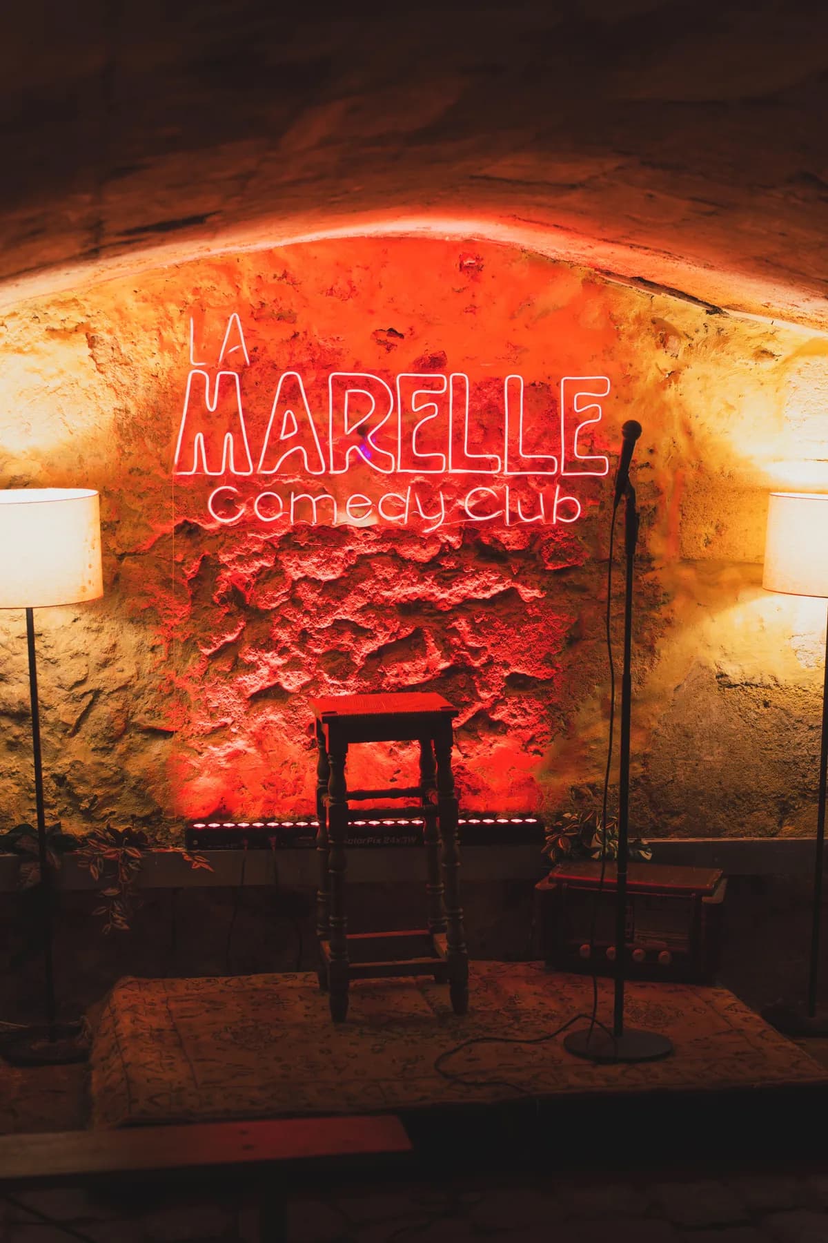 Format comedy club privatisé à Bordeaux — La Marelle Scène format comedy club avec enseigne néon La Marelle, micro et tabouret — privatisation à Bordeaux