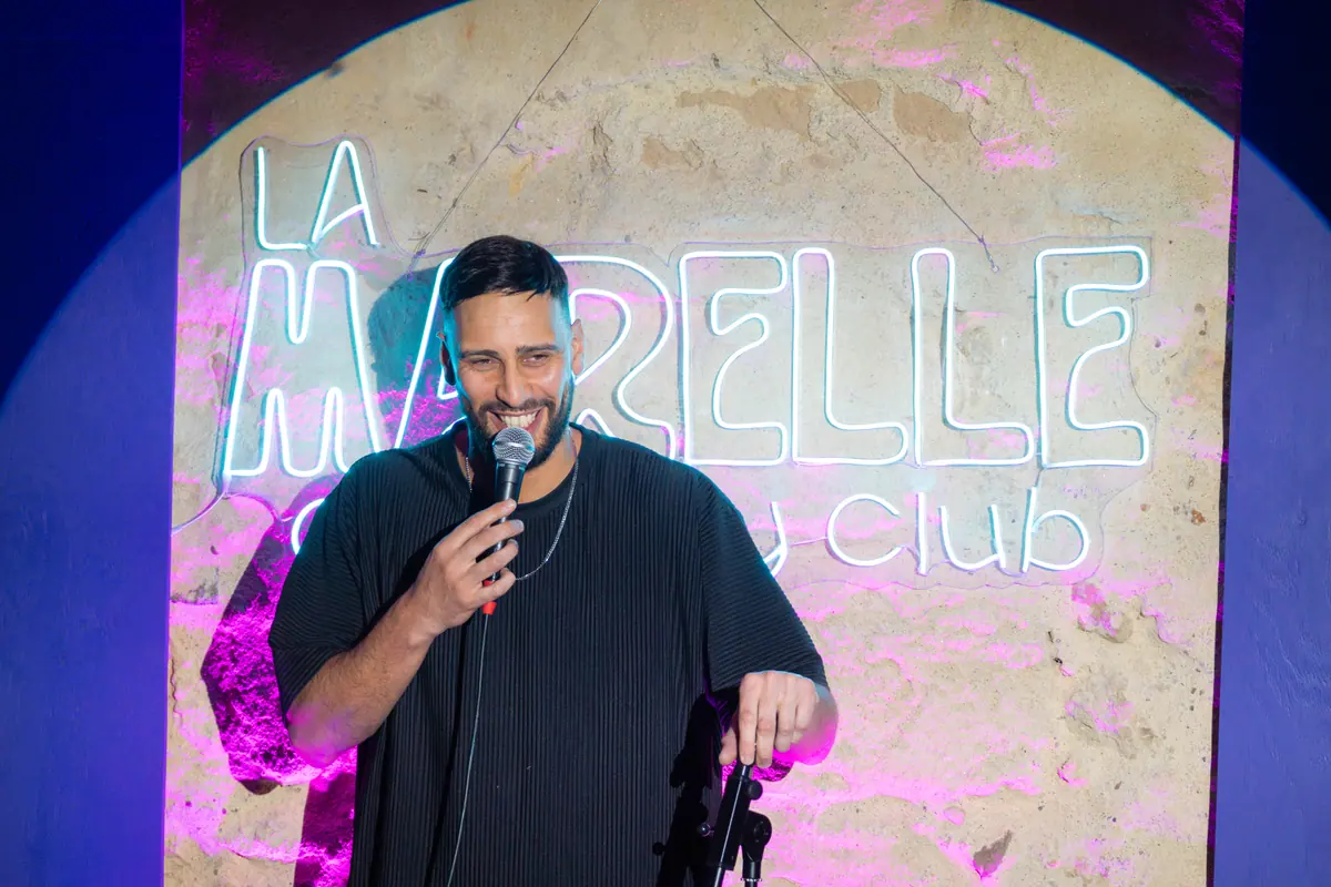 Comédien stand-up devant l'enseigne néon LA MARELLE Comedy Club — Marelle Bleue, Pas de Lune Bordeaux